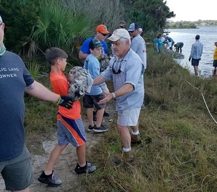 Group of volunteers work along a grassy riverbank to clean up debris